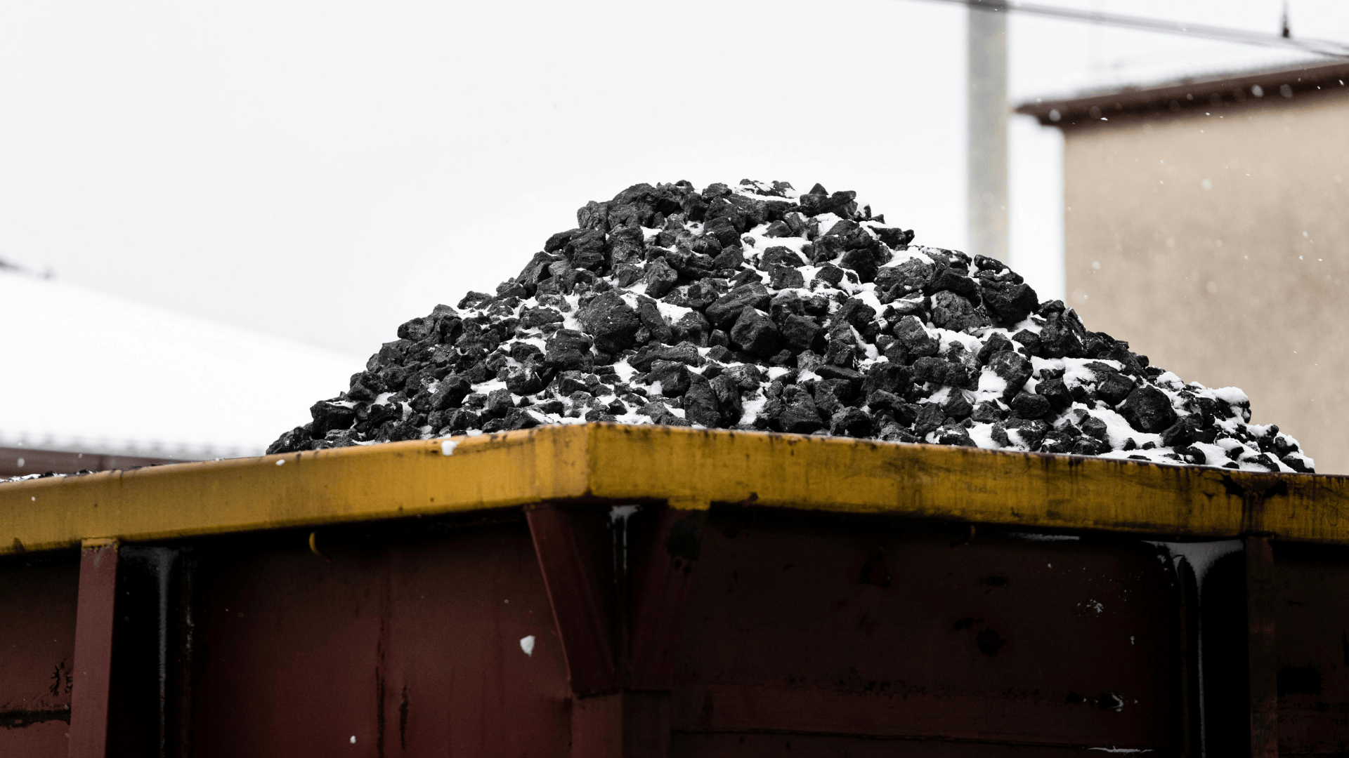 Pile of black coal covered with snow in a yellow industrial container outdoors.