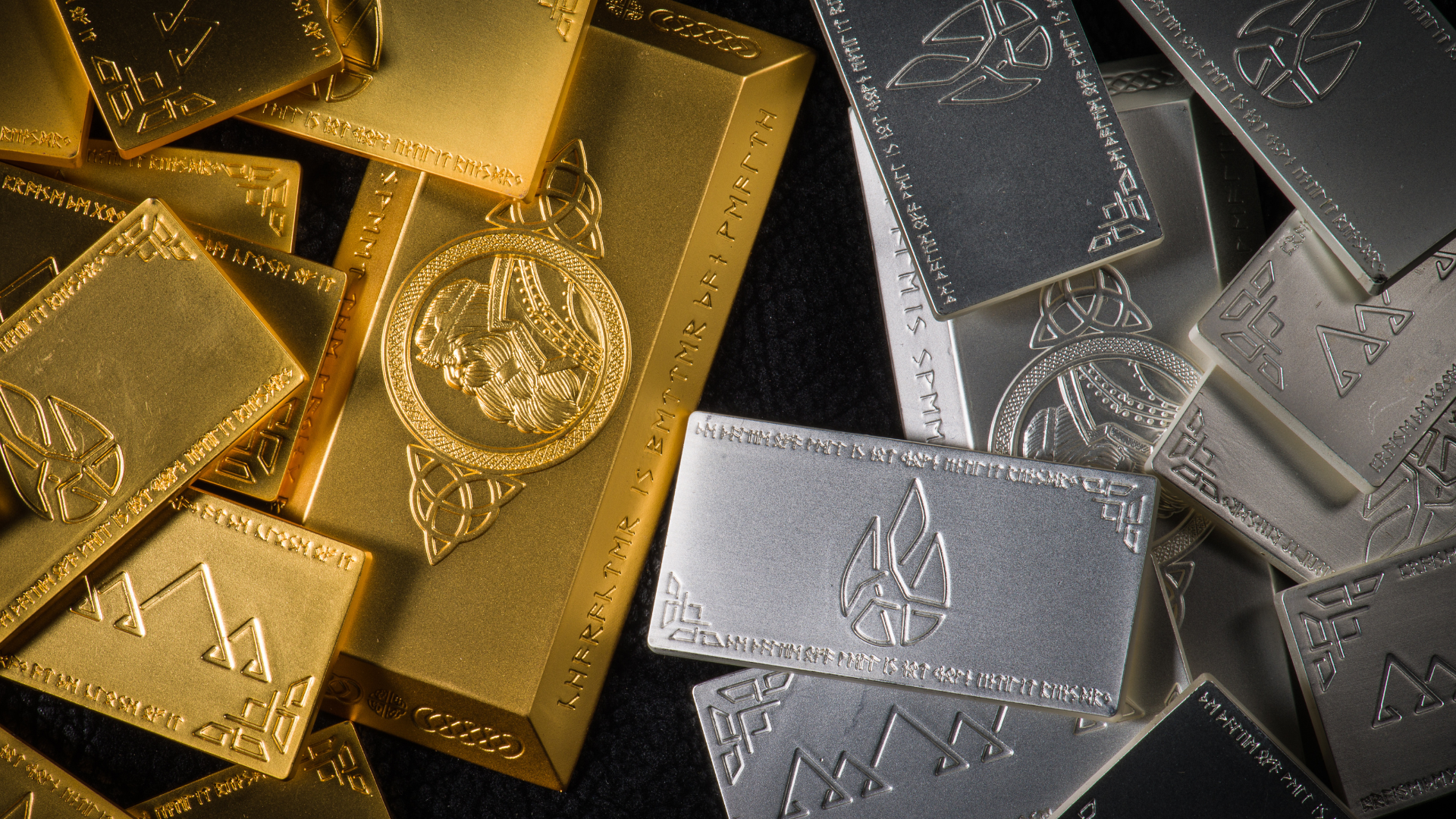 Close-up of stacked gold and silver bullion bars with intricate engraved designs on a dark background.