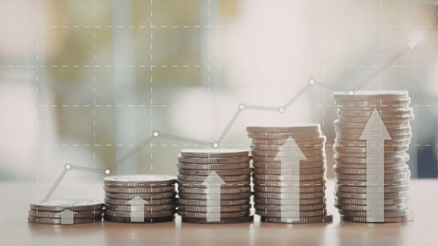 Stacked coins with upward arrows and growth chart representing rising financial markets and investment growth