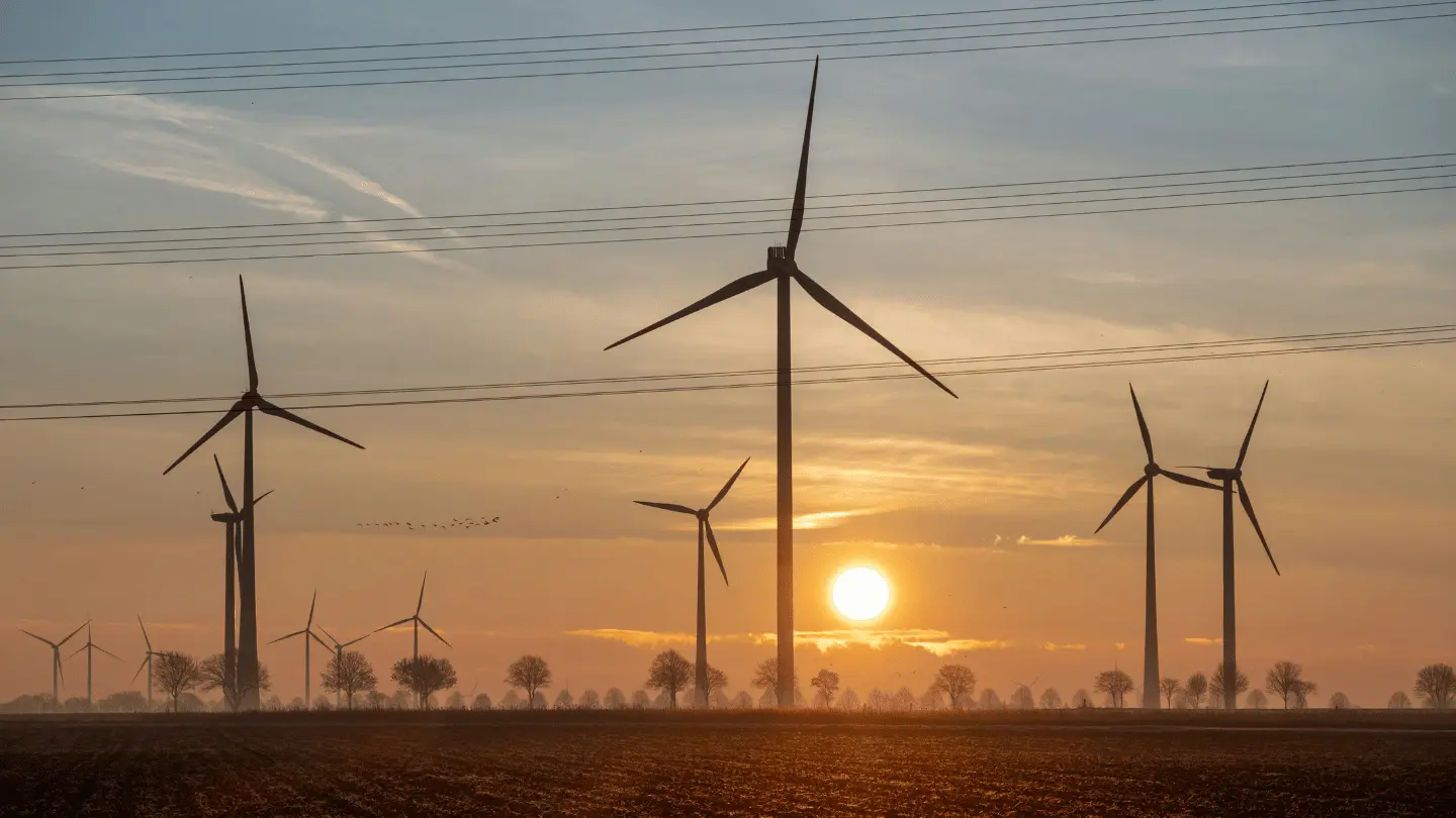 Wind turbines standing across an open field at sunset, generating renewable energy under an orange evening sky.