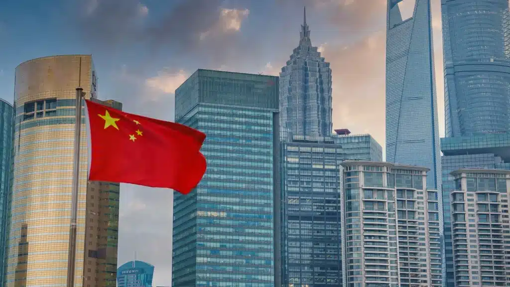 Chinese flag waving with modern skyscrapers and financial district skyline in the background.